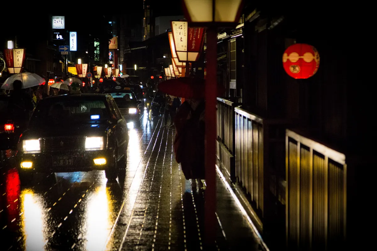 Eine breite gepflasterte Straße, gesäumt von traditionellen hölzernen Stadthäusern in Gion, Kyoto, an einem hellen Tag