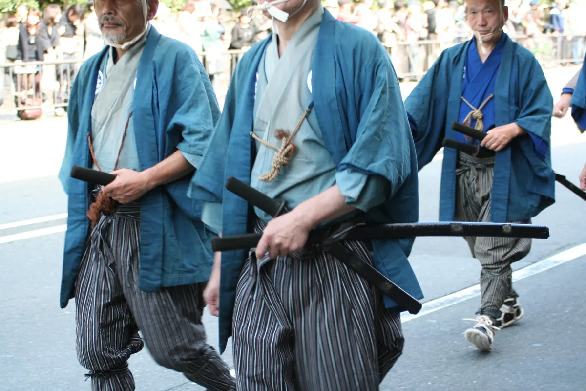 Männer in Gewändern aus der Samurai-Zeit mit Schwertern am Gürtel bei einem Festumzug in den Straßen von Kyoto